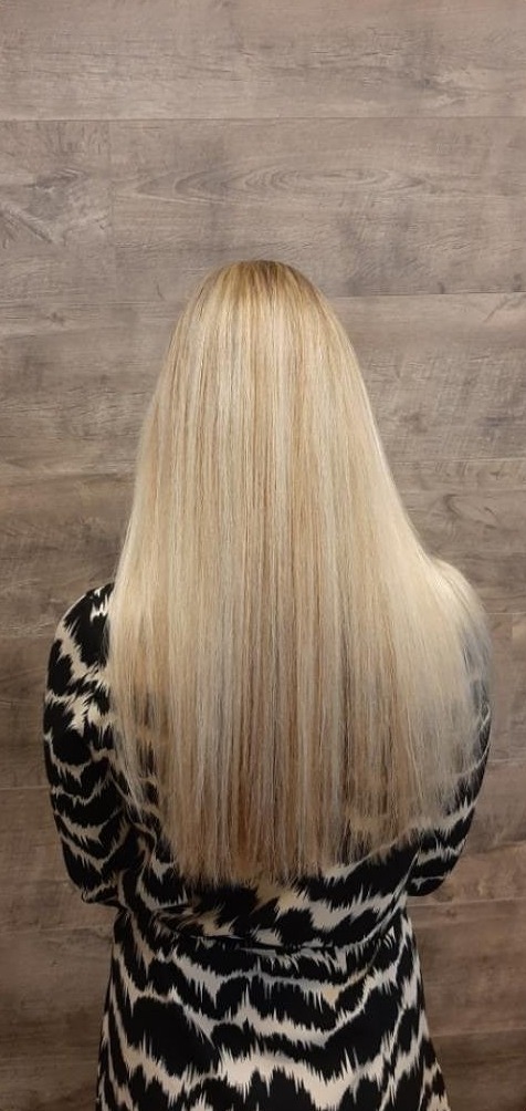 Lang, glad blond haar van een klant, van achteren gezien voor een houten wand
